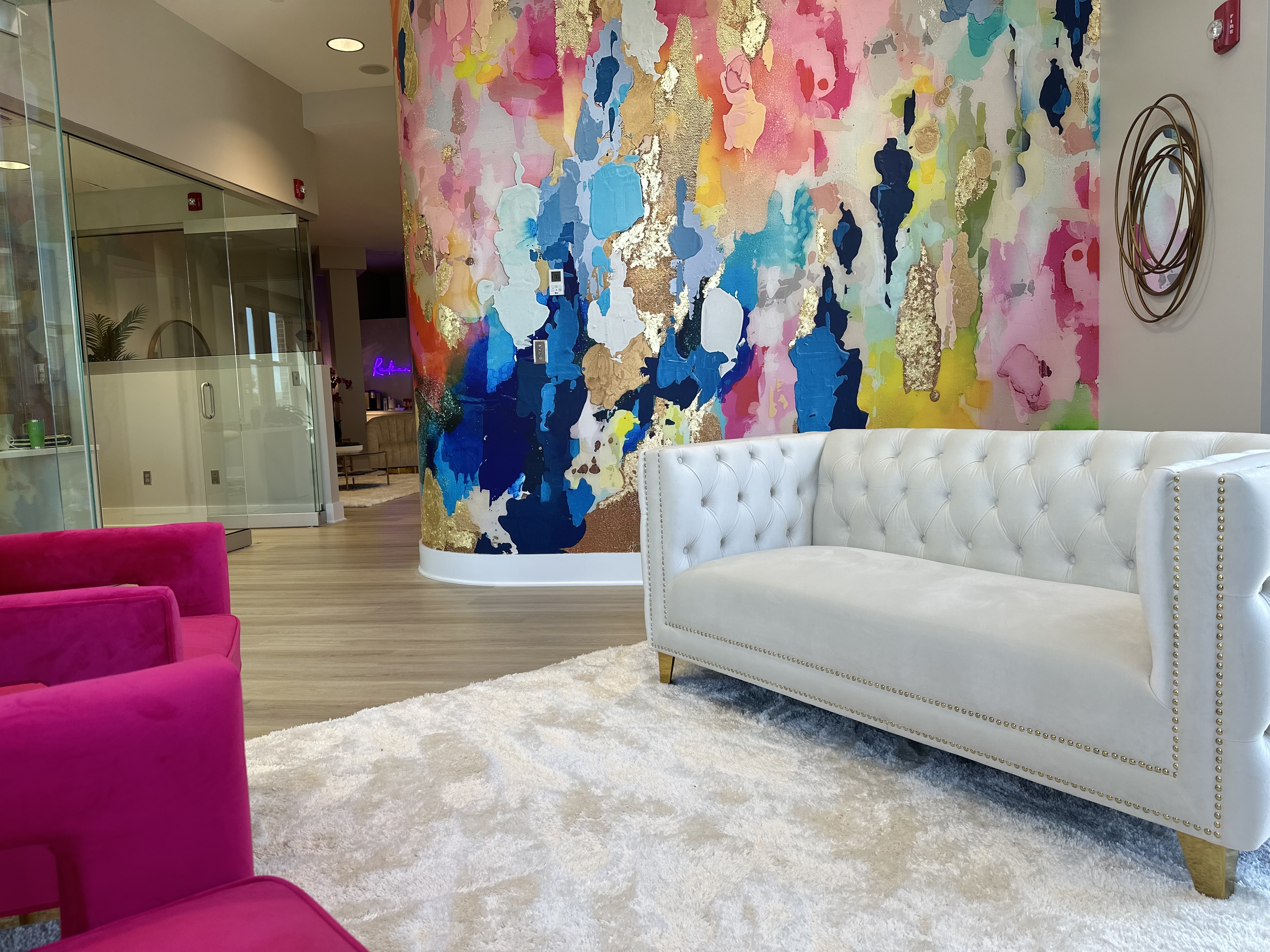 Inside Radiant Med Spa featuring a luxury lobby with a colorful gold-accented mural, white tufted sofa, and pink velvet chairs
